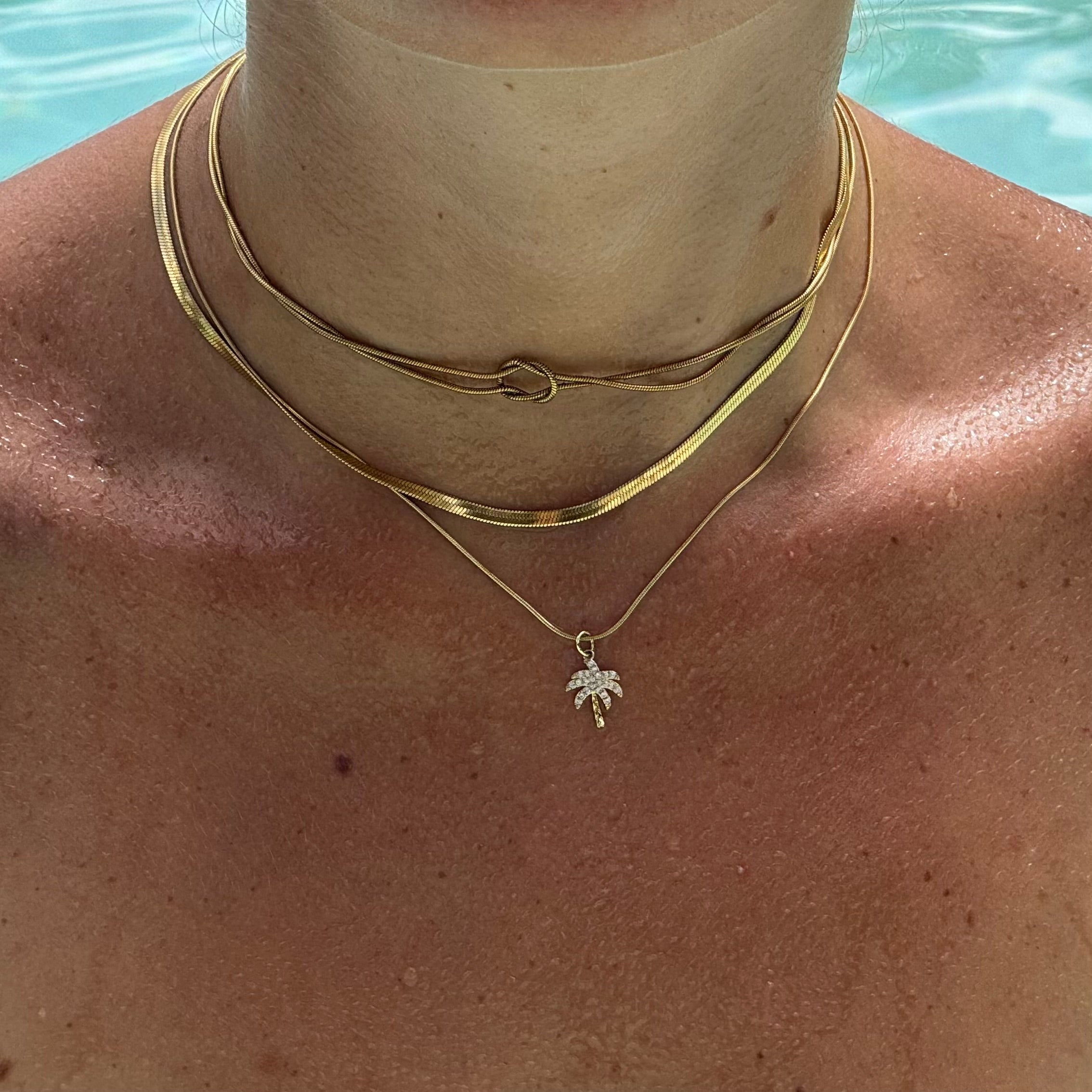 Hals im Pool mit Palmen-Anhänger aus 18l vergoldetem Metall, besetzt mit Zirkonia-Steinen, kombiniert mit einer Schlangenkette aus 14k vergoldetem Edelstahl. Sommerlicher Schmuck-Look mit tropischem Flair. 