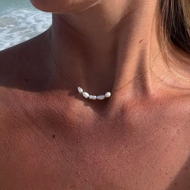 Hals mit feiner Perlenkette aus echten weißen Süßwasserperlen, kombiniert mit 14kvergoldeten Edelstahl-Elementen. Sommerlicher Schmuck-Look am Meer mit natürlicher Eleganz. 