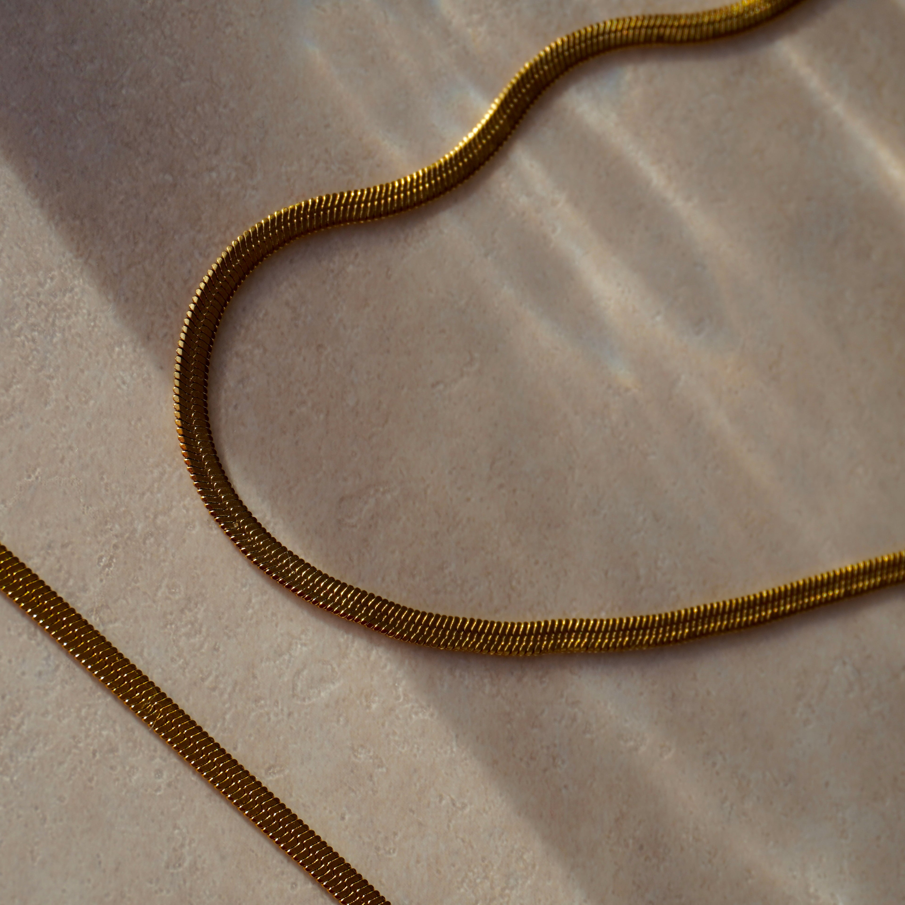 Schlangenkette aus 14k vergoldetem Edelstahl auf hellem Untergrund. Glänzendes, geschmeidiges Design, ideal für elegante Layering-Looks.